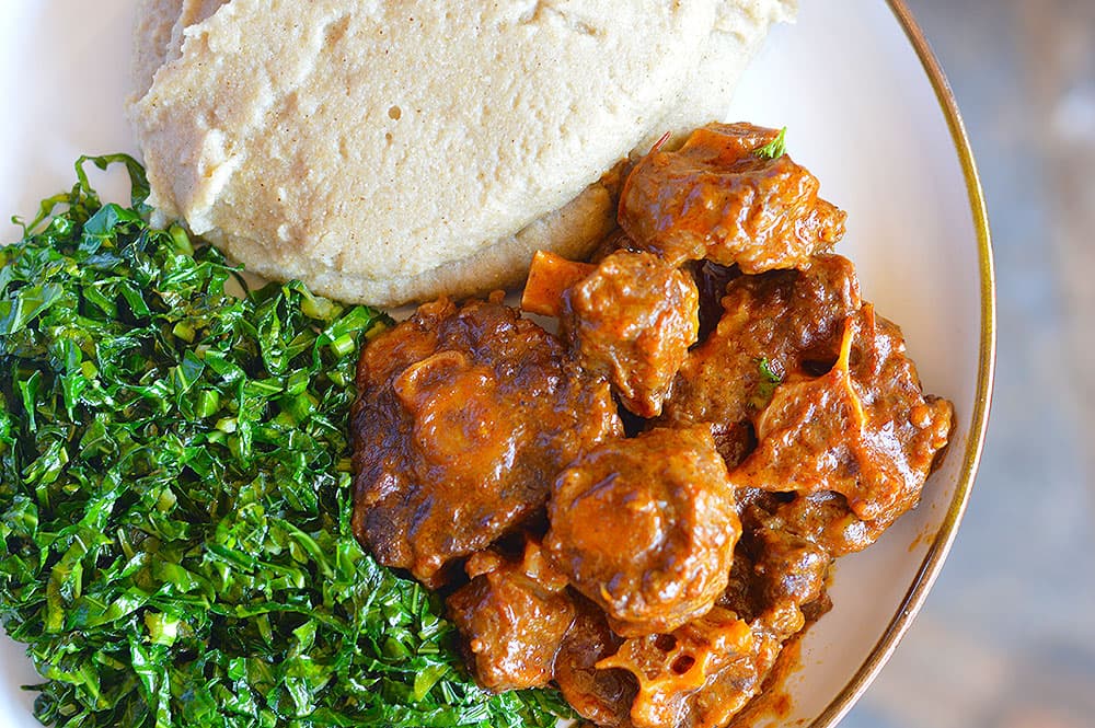 A plate of sadza with oxtail and vegetables